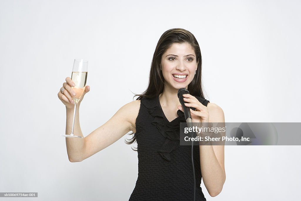 Young woman holding up champagne with microphone on white background