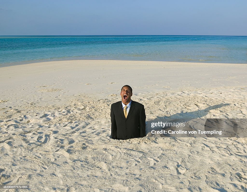 Businessman trapped in hole in sand, mouth open