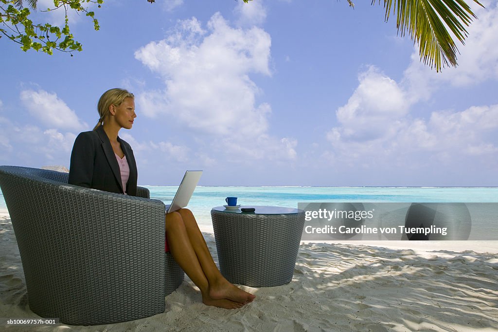 Businesswoman using laptop on beach