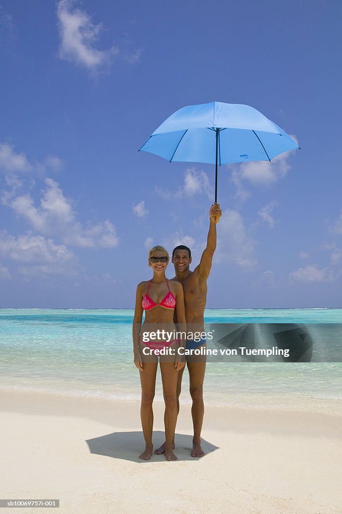 Young couple on beach with umbrella, smiling