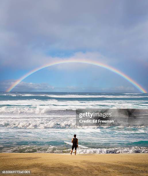 surfer with surfboard on beach, looking at view - beach sand and water hawaii stock-fotos und bilder