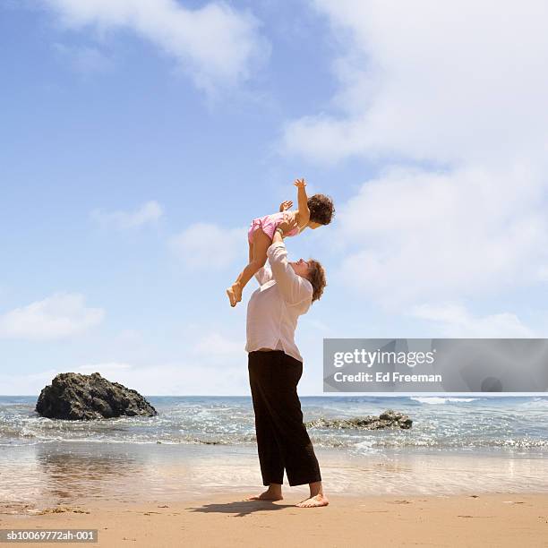 mother holding daughter (2-3) up in airplane position on beach - 飛行機のまね ストックフォトと画像