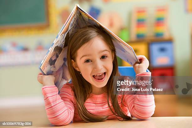 girl (4-5) holding open book on head, smiling, portrait - portare sulla testa foto e immagini stock