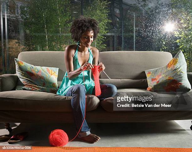 young woman knitting on sofa in livingroom - a maglia foto e immagini stock