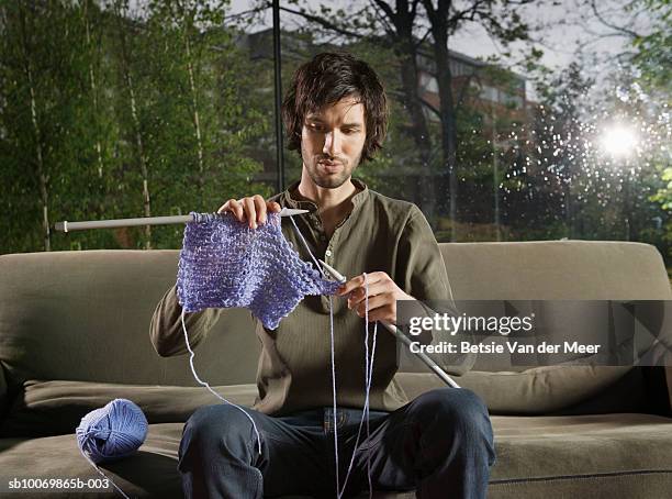 young man knitting on sofa in livingroom - knitting stock pictures, royalty-free photos & images