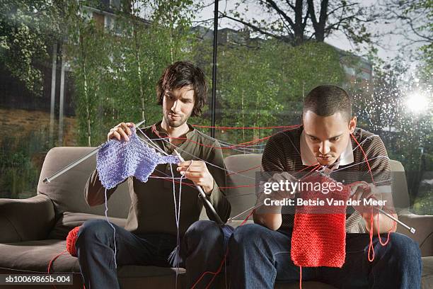 two young men knitting on sofa in living room - man knitting stock pictures, royalty-free photos & images