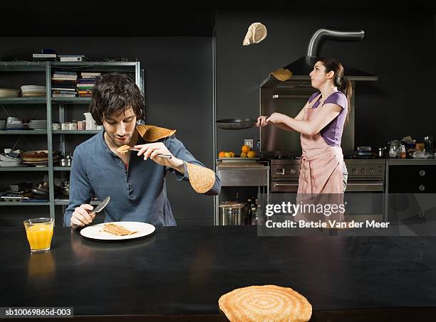man eating pancake, while woman turning them in pan - pancake day foto e immagini stock