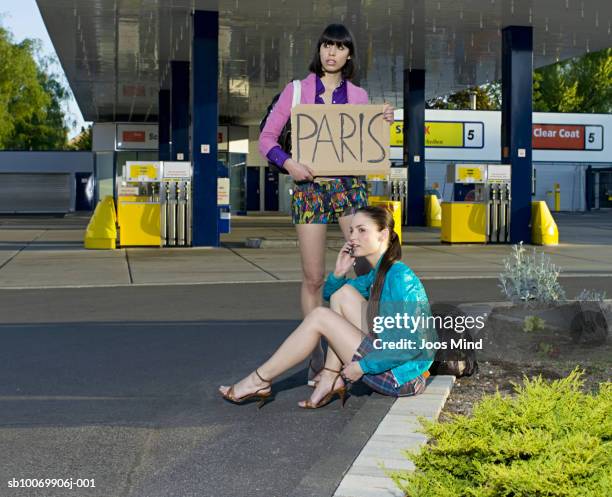 two young women hitchhiking at petrol station - hitchhike stock-fotos und bilder