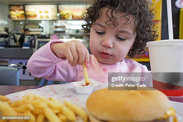 girl (2-3) sitting at table eating french fries, close-up - fast food french fries stock-fotos und bilder
