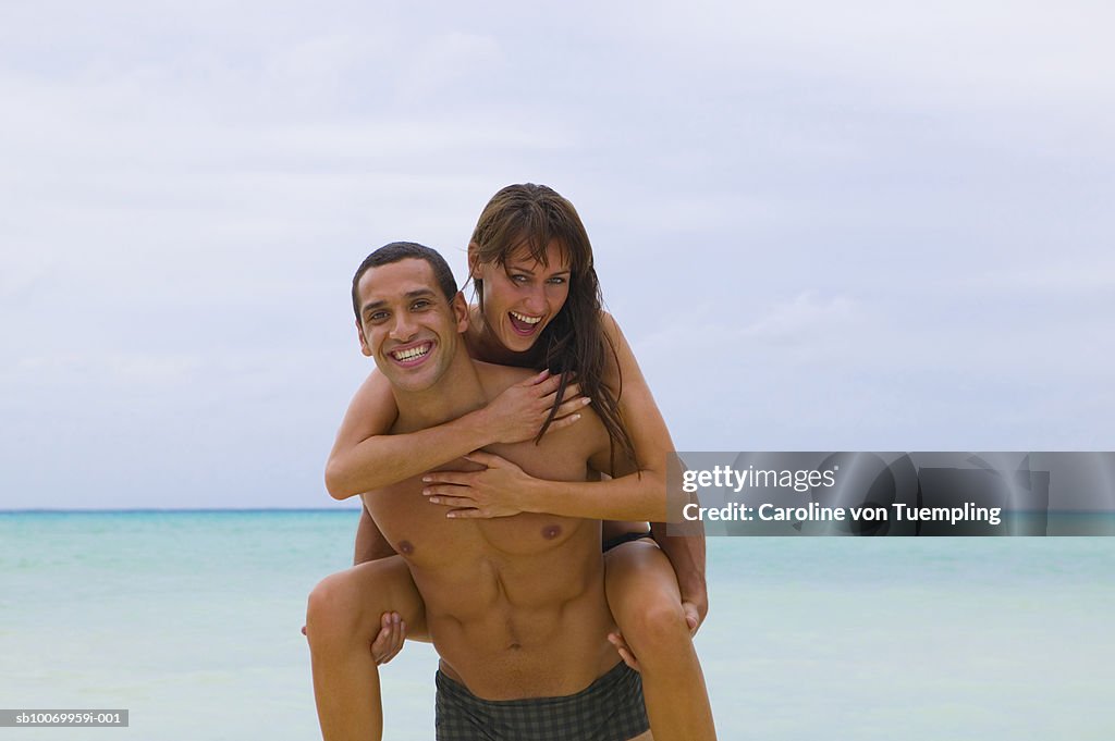 Man giving woman piggy back ride on beach, smiling, portrait