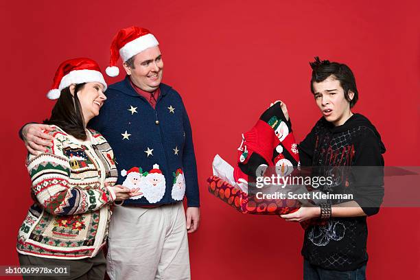 teenage boy (12-13) receiving christmas sweater gift from parents, studio shot - embarrased dad stockfoto's en -beelden