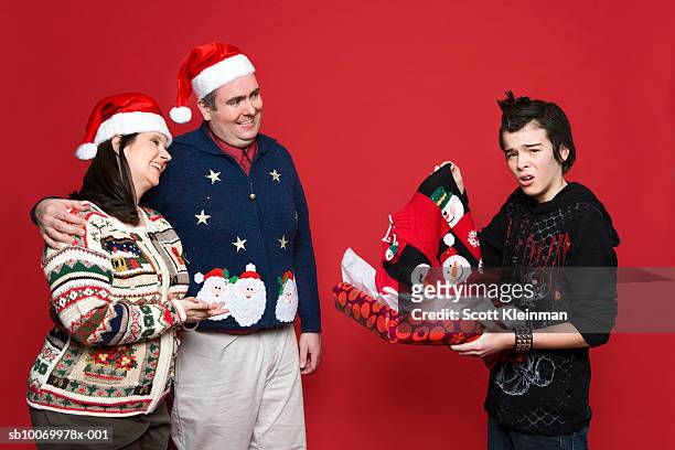 teenage boy (12-13) receiving christmas sweater gift from parents, studio shot - fealdade imagens e fotografias de stock