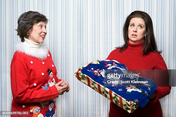 mature daugther receiving christmas sweater gift from mother, studio shot - disappointment gift stock pictures, royalty-free photos & images