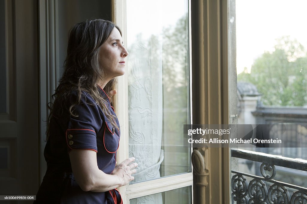 Mid adult woman looking out window of apartment