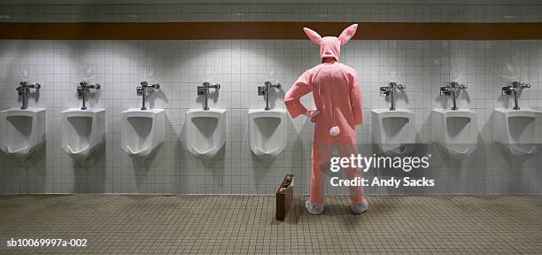 man wearing rabbit costume at urinal, rear view (digital composite) - pistas stockfoto's en -beelden