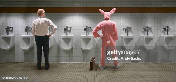 two men standing at urinal, one in rabbit costume, rear view (digital composite) - pistas stockfoto's en -beelden