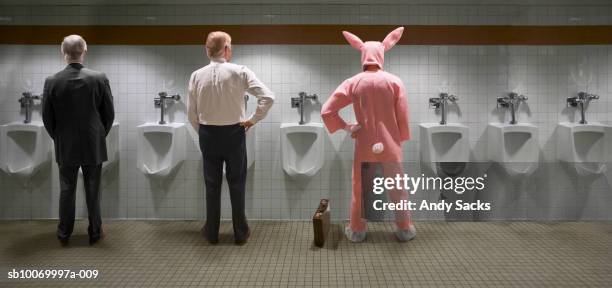 three men standing at urinal, one in rabbit costume, rear view (digital composite) - chelsea pensionär stock-fotos und bilder