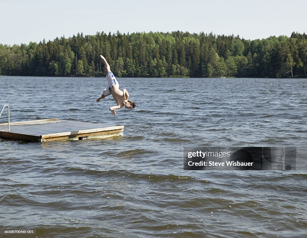 Young man jumping off jetty into lake