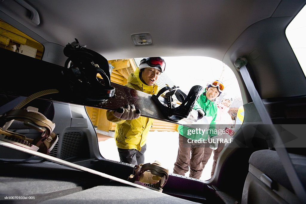 People putting snowboards into car trunk