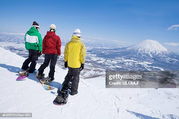 three snowboarders on edge of slope, rear view - niseko stock pictures, royalty-free photos & images