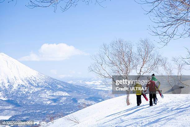 three snowboarders walking on slope, rear view - niseko stock pictures, royalty-free photos & images