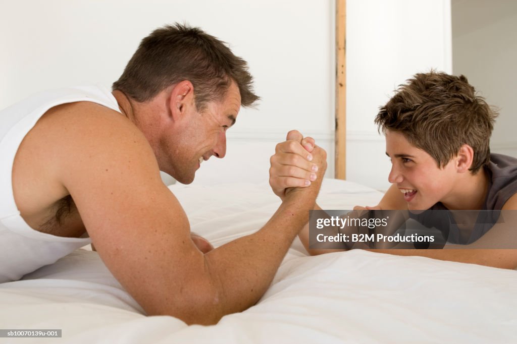 Father and son (12-13) arm wrestling on bed