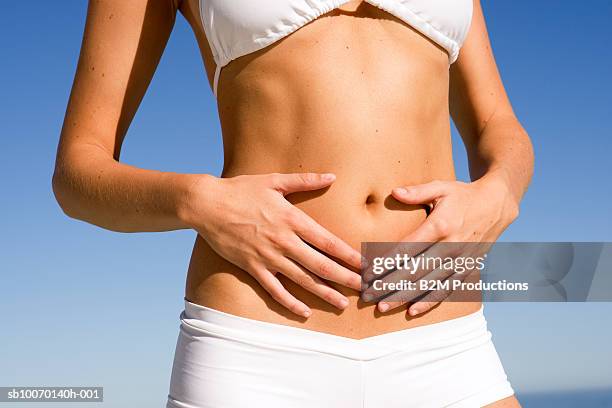 young woman in bikini touching her stomach, mid section - halbbekleidet stock-fotos und bilder