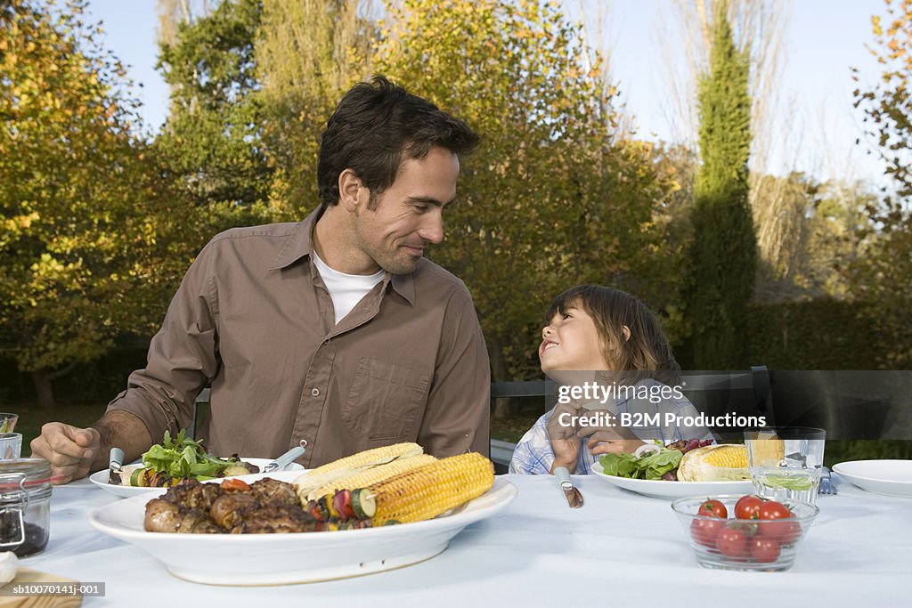 Father and son (3-4) sitting at table in garden and looking in eyes