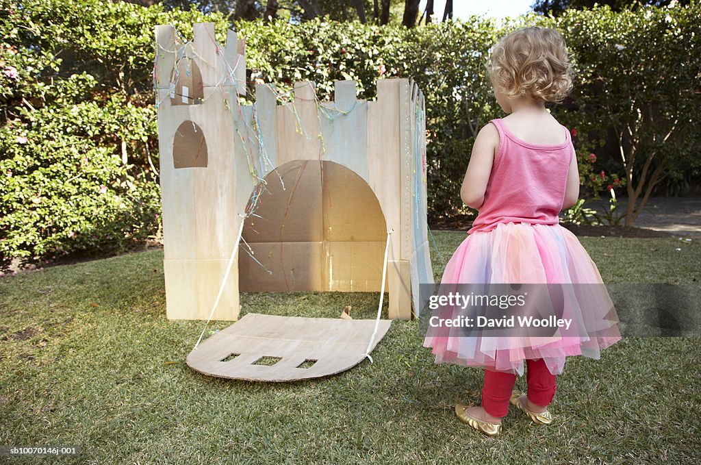 Young girl (12-17 months) looking at cardboard castle in garden