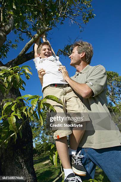 boy (10-11) playing with his father around a tree - genderblend stock-fotos und bilder