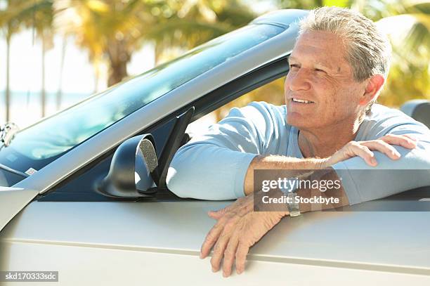 man sitting in a convertible car leaning on the door - door stockfoto's en -beelden