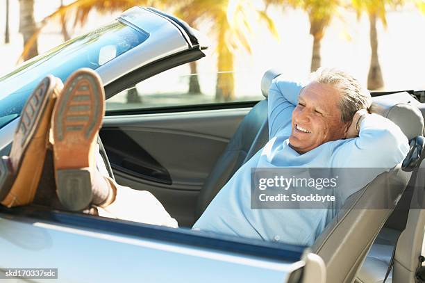 man relaxing in a convertible car with his feet leaning on the door - door stockfoto's en -beelden