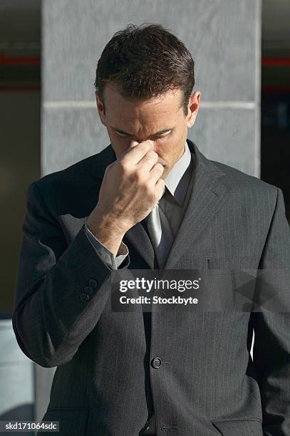 businessman pinching his nose with his head lowered - pinching nose stockfoto's en -beelden