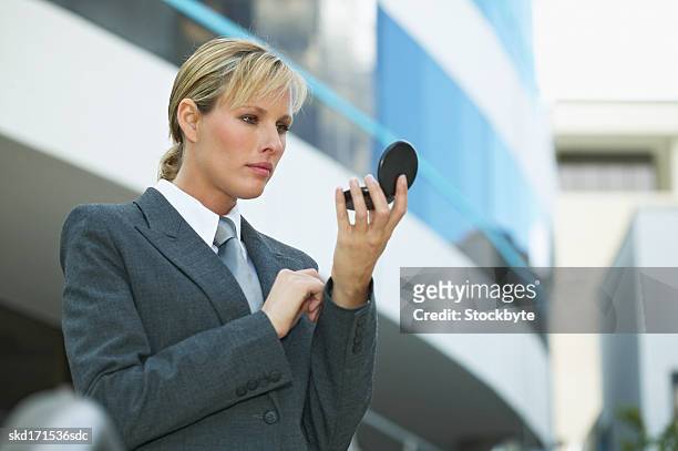businesswoman checking her appearance in a compact mirror - compact mirror stockfoto's en -beelden