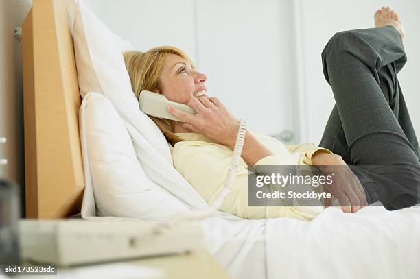 businesswoman lying on a bed talking on the telephone - landline phone home foto e immagini stock