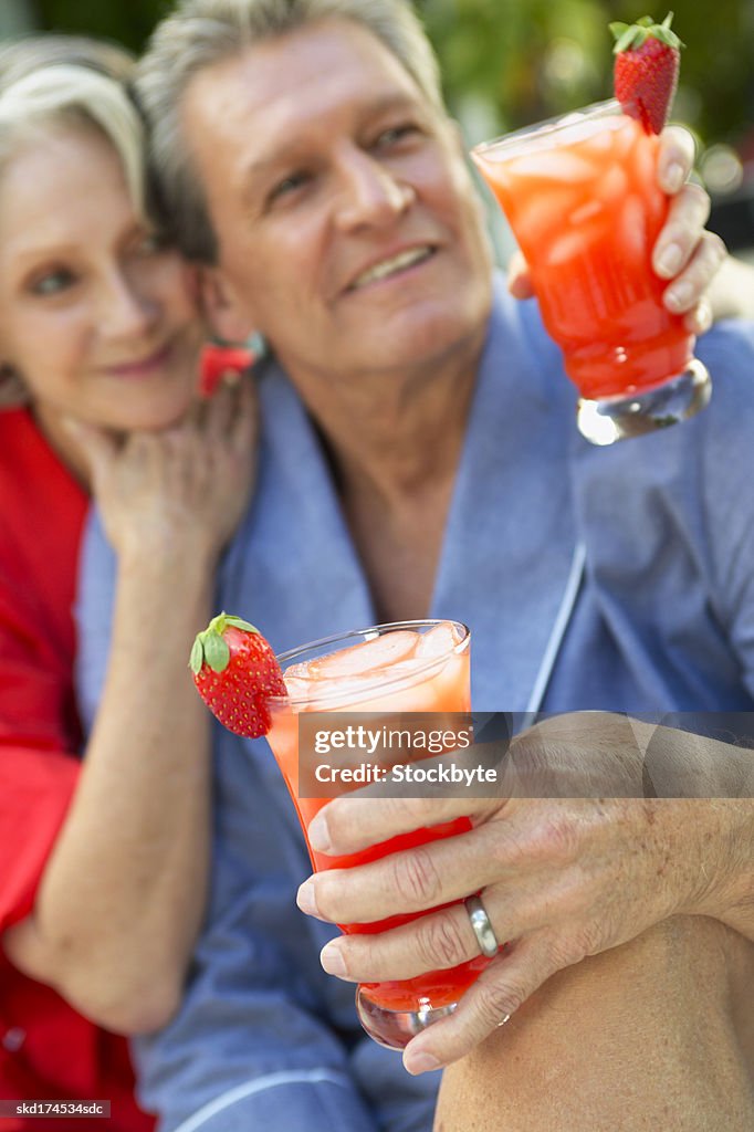 Couple hugging holding cocktails sitting by swimming pool