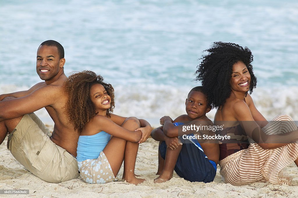 Portrait of son (10-11) and daughter (10-11) sitting on the beach with their mother and father