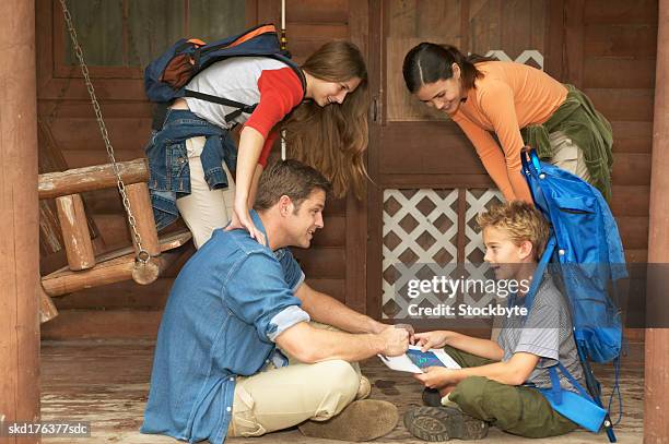 side view of a father and son (10-11) sitting on the floor boy is wearing backpack mother and sister (15-16) standing - is stock pictures, royalty-free photos & images