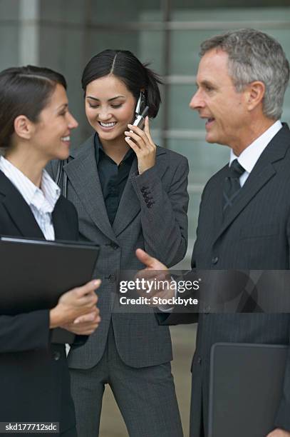 two business executives talking in the foreground and another businesswoman talking on mobile phone in the background - aother stock pictures, royalty-free photos & images