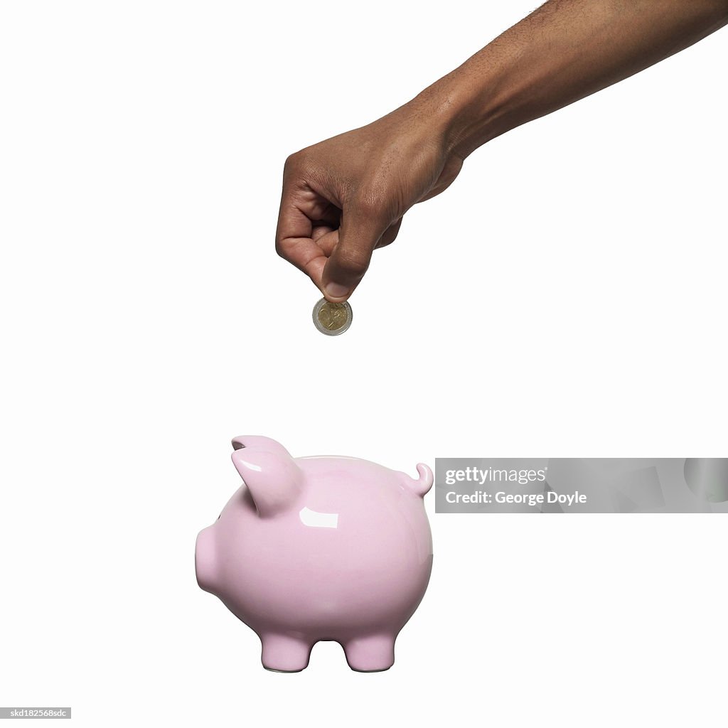 Close-up of male hand putting coins into piggy bank