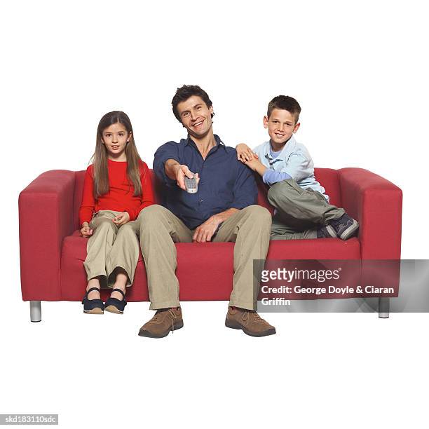portrait of a father holding remote control and two children (10-12) sitting on couch - control photos et images de collection