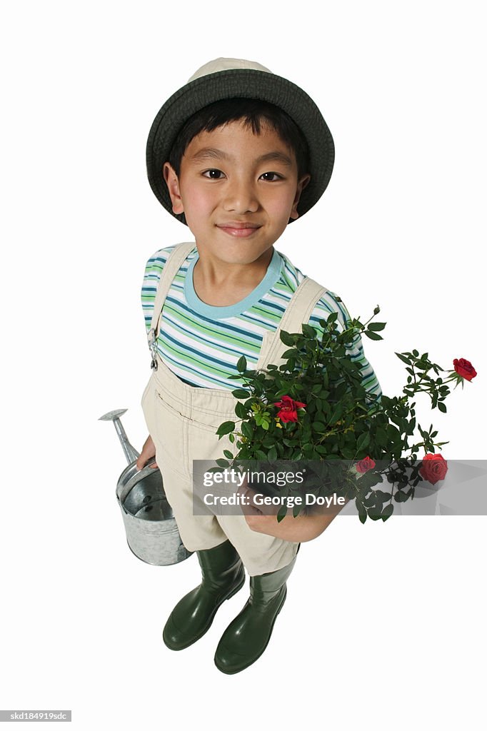 Elevated view of a boy (8-9) holding a watering can and a plant