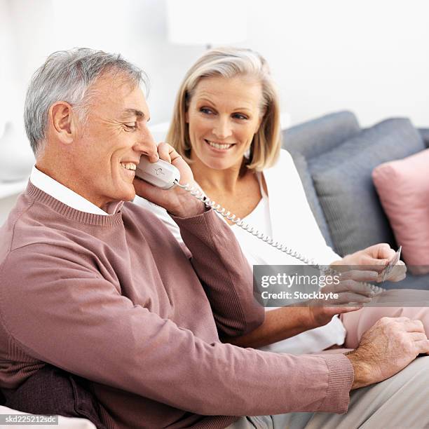 close-up of mature couple sitting on sofa talking on telephone and holding credit card - landline phone home stock pictures, royalty-free photos & images