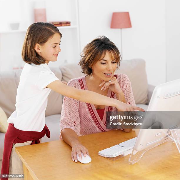 mother using a computer with her daughter (9-10) - renversement des rôles photos et images de collection