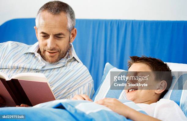 close-up of father reading story to son (10-11) - bedtime stories stock-fotos und bilder