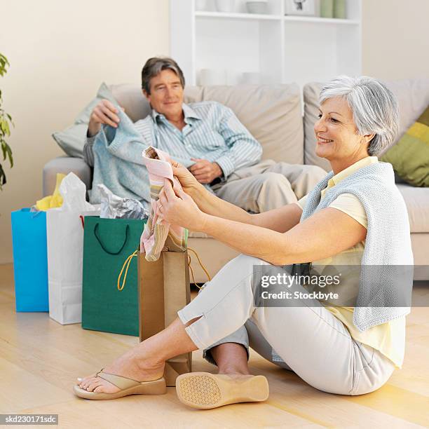 mature couple sitting in living room with woman looking at clothes - living stock-fotos und bilder