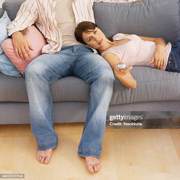 front view of young couple sitting on sofa and holding remote control - control photos et images de collection