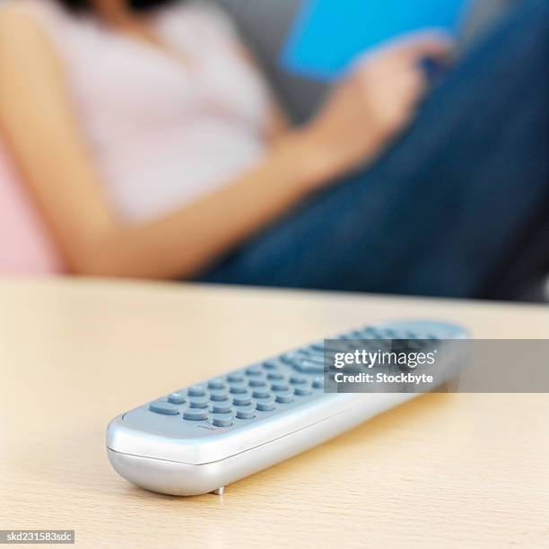 young woman sitting on sofa with remote control on coffee table - control photos et images de collection