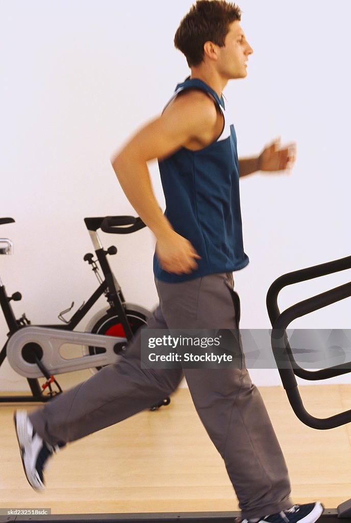 Side profile of a young man running on a treadmill in a gym