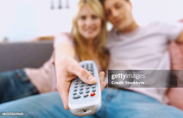 close-up of a young couple sitting on a couch with a remote control (blurred) - control photos et images de collection